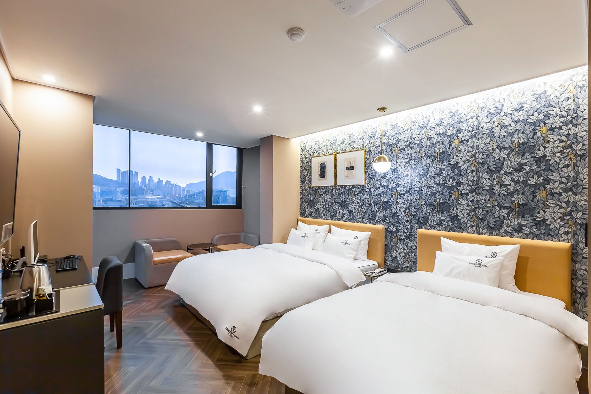 Une chambre d’hôtel avec deux lits, un bureau, une chaise et une grande fenêtre donnant sur la ville.