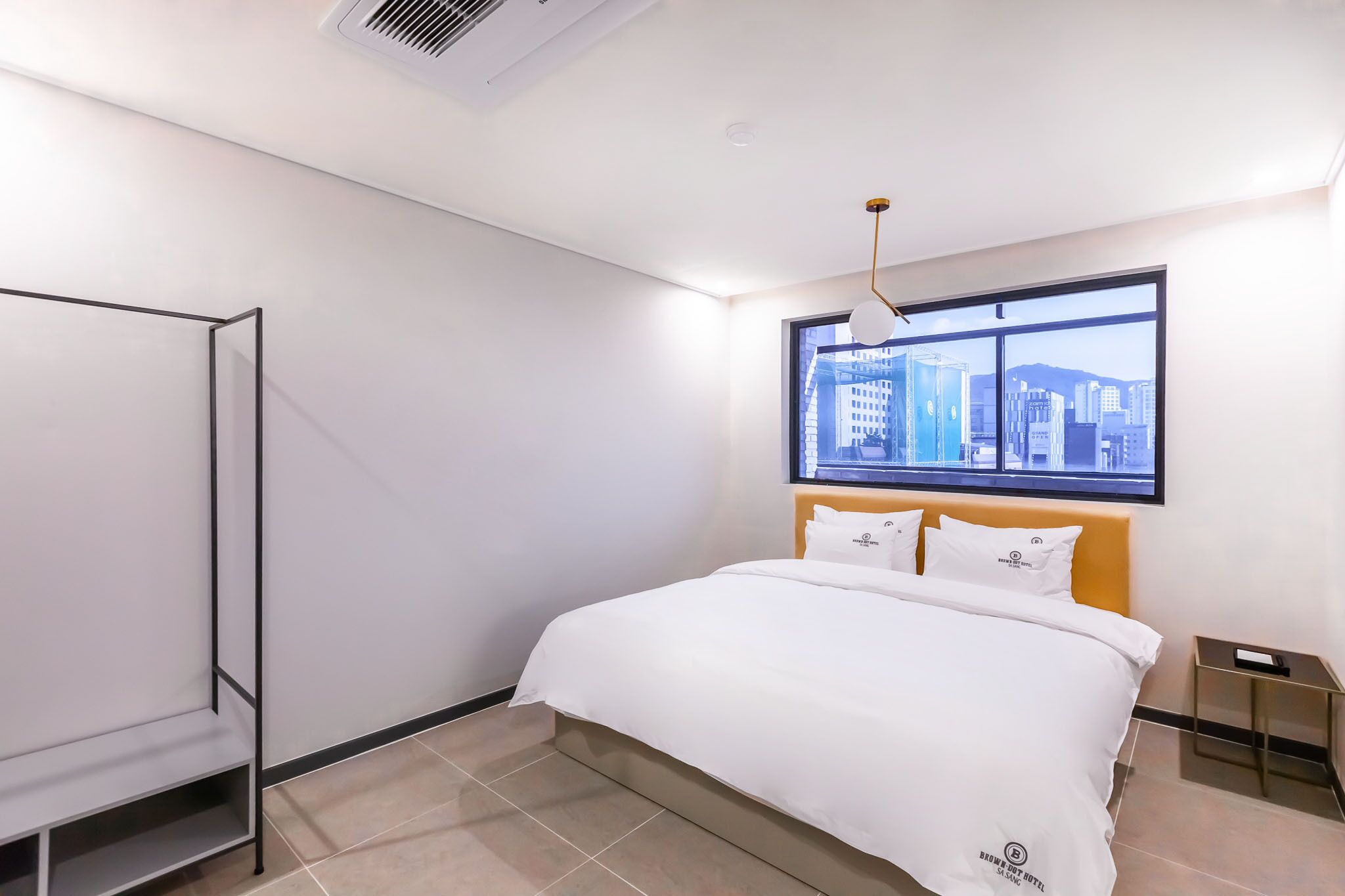 Una camera d'albergo con un letto, un comodino, una finestra che si affaccia sulla città e uno schermo per proiettore.