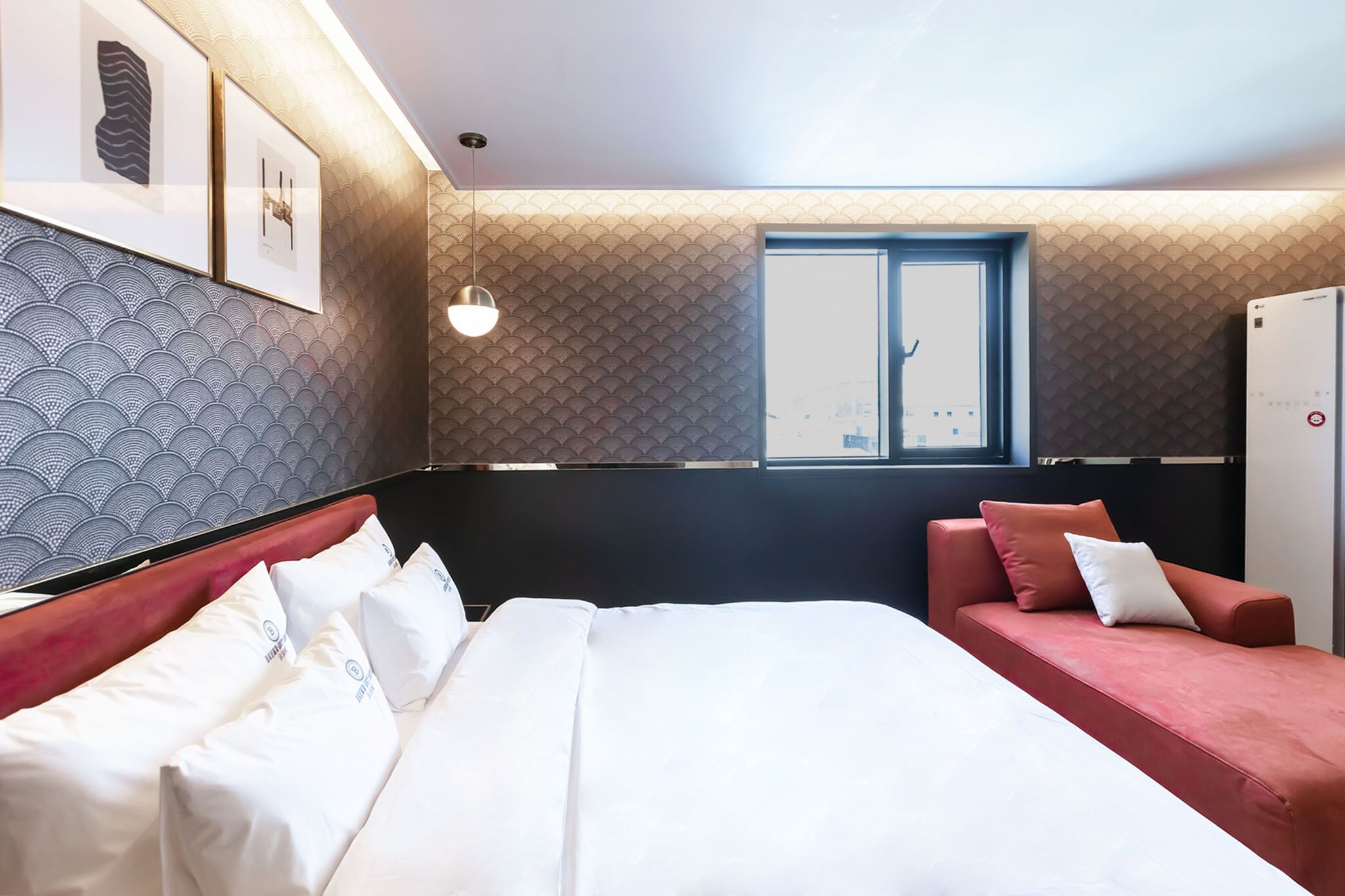 Una habitación de hotel con una cama, un sofá rojo, una ventana y obras de arte colgadas en la pared.