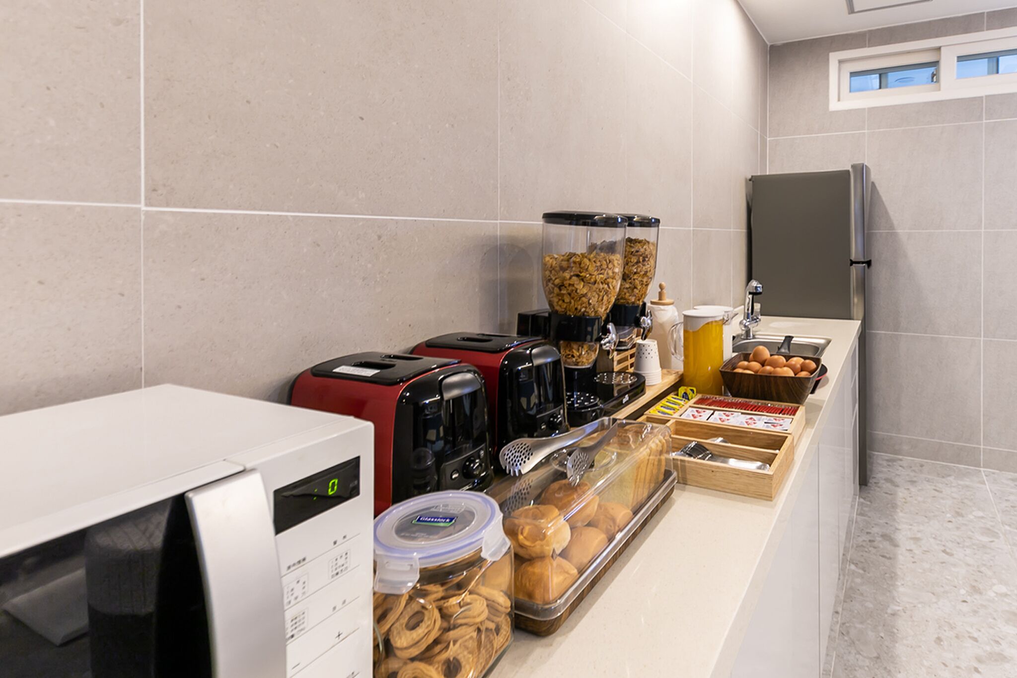 A breakfast bar with coffee makers, a microwave, and various food items like pastries and eggs.