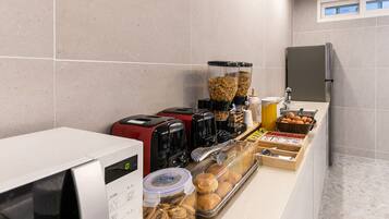 A breakfast bar with coffee makers, a microwave, and various food items like pastries and eggs.