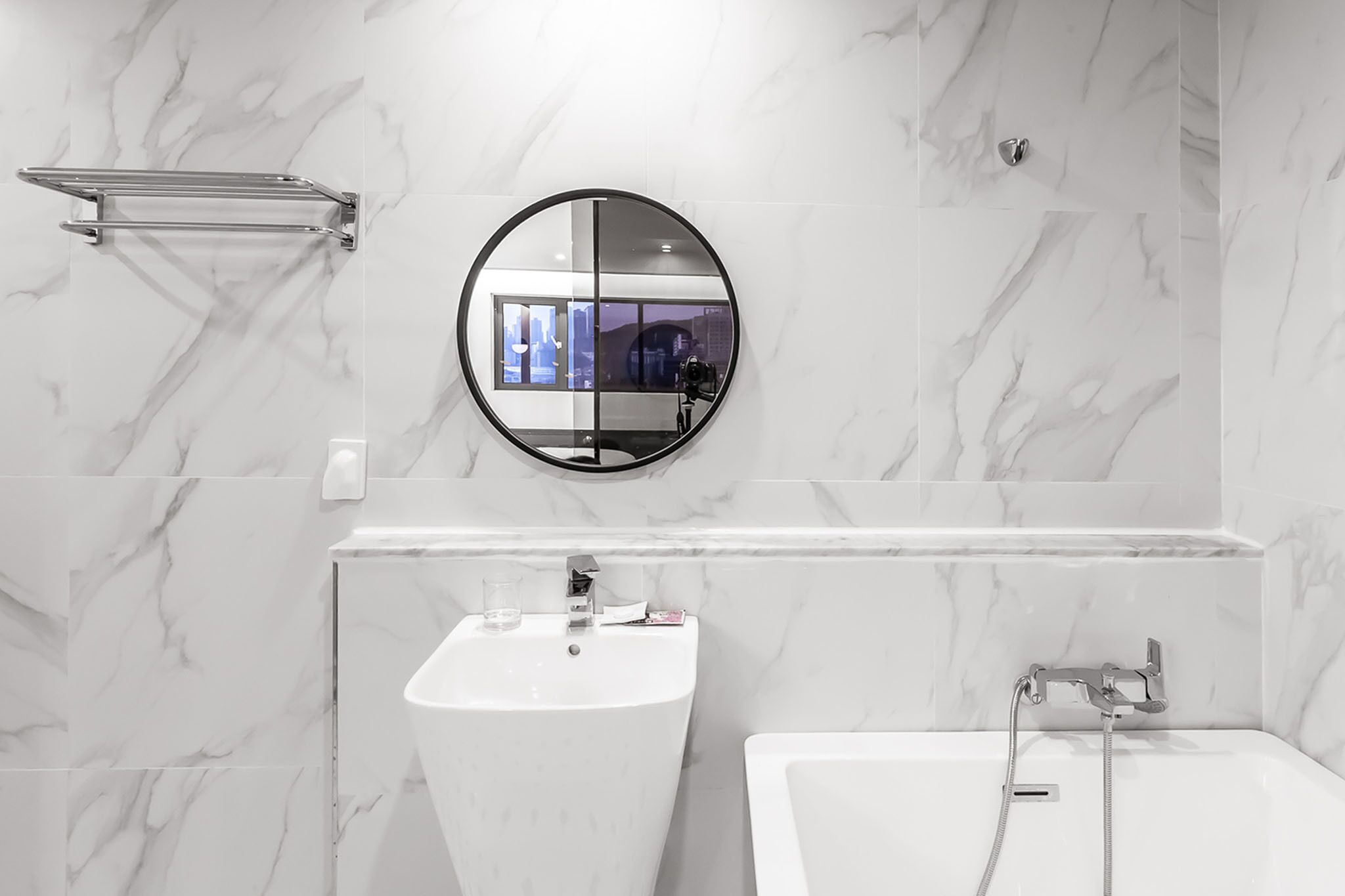 Une salle de bain moderne avec un pare-baignoire en marbre, un miroir rond, un lavabo et une baignoire.