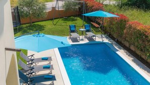 Una piscina rectangular con borde azul, rodeada de sillas de descanso y sombrillas.