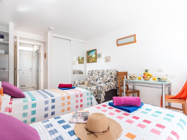 A bedroom with two beds, a chair, a table with fruit, and a mirror.