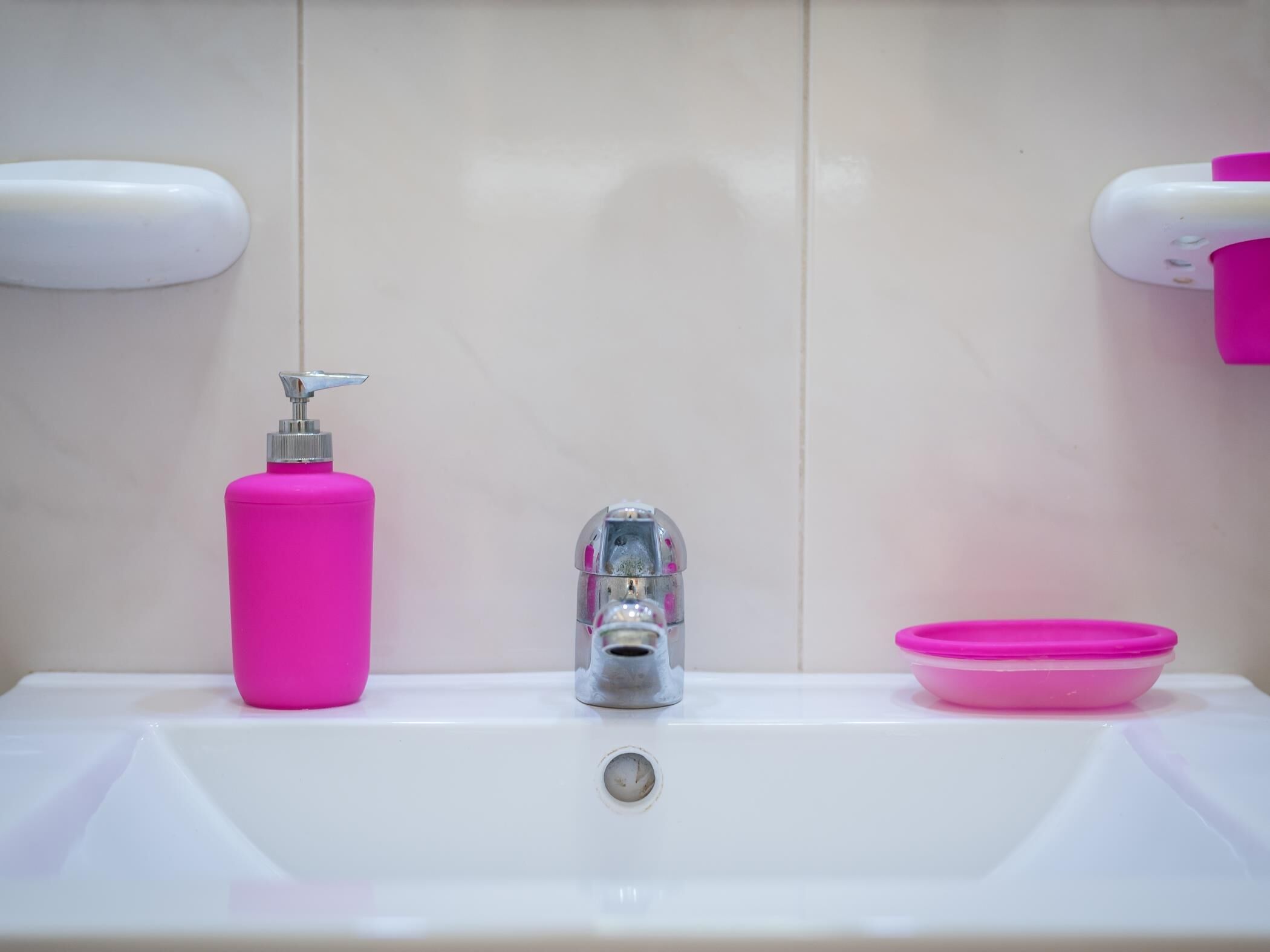 Un lavabo de salle de bain avec un distributeur de savon rose, un robinet et un bac rose.