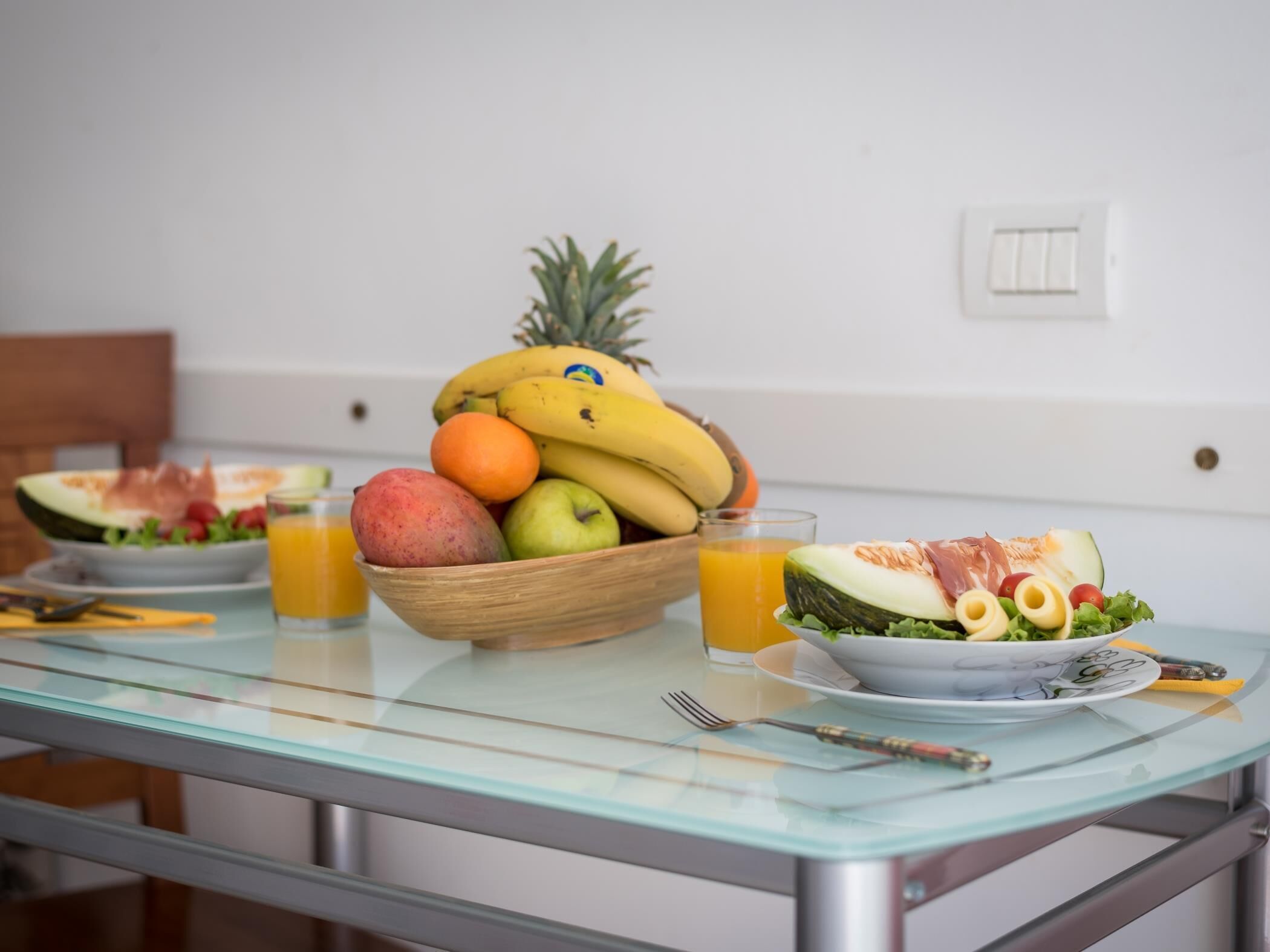 A dining table with a fruit bowl, a plate of salad, and a glass of orange juice.