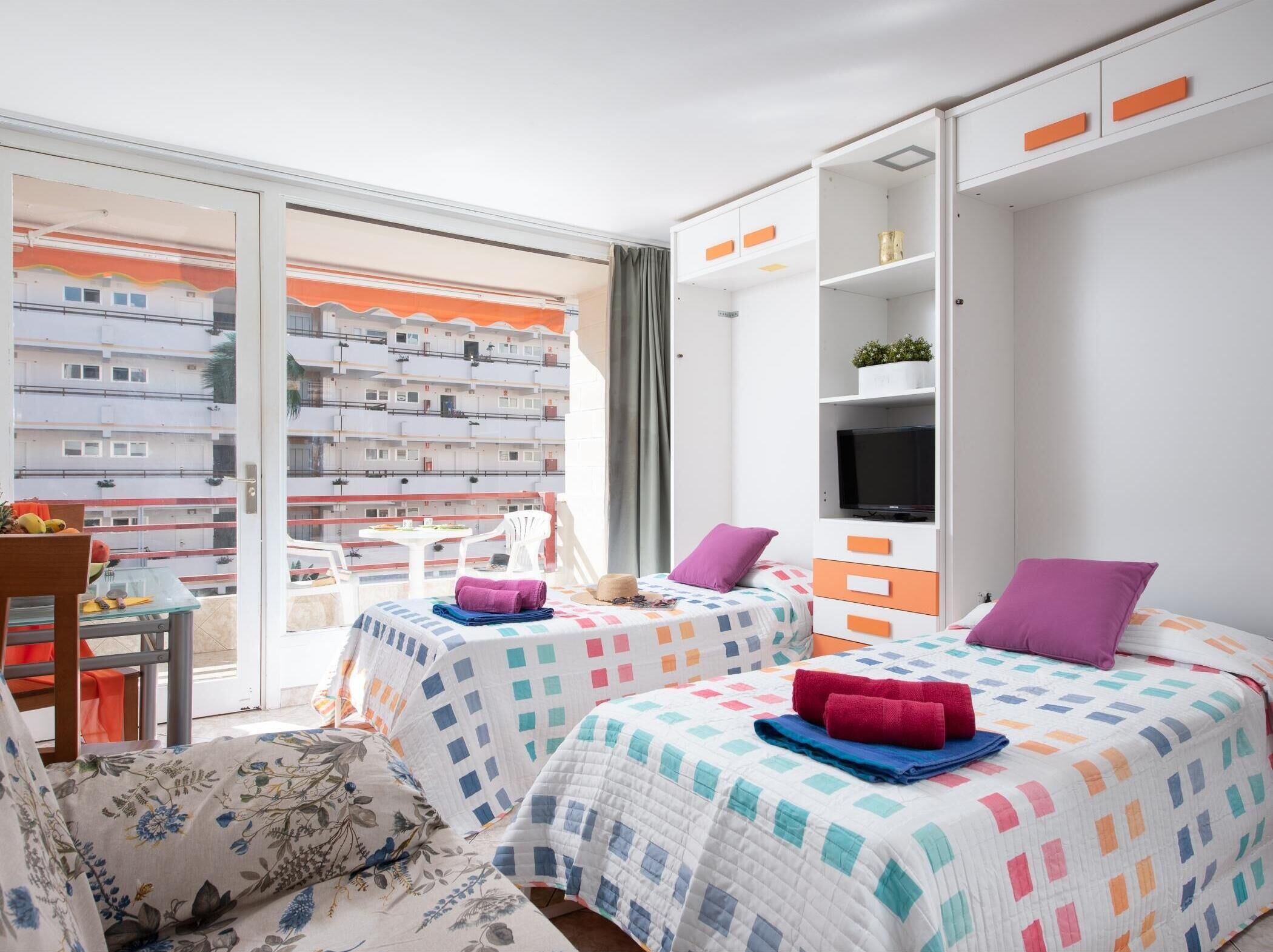 Ein Hotelzimmer mit zwei Betten, einem Fernseher und einem Balkon mit Blick auf die Stadt.