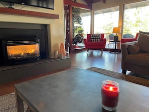 Uma sala de estar com lareira, um sofá vermelho, um sofá bege e uma mesa com uma vela acesa.