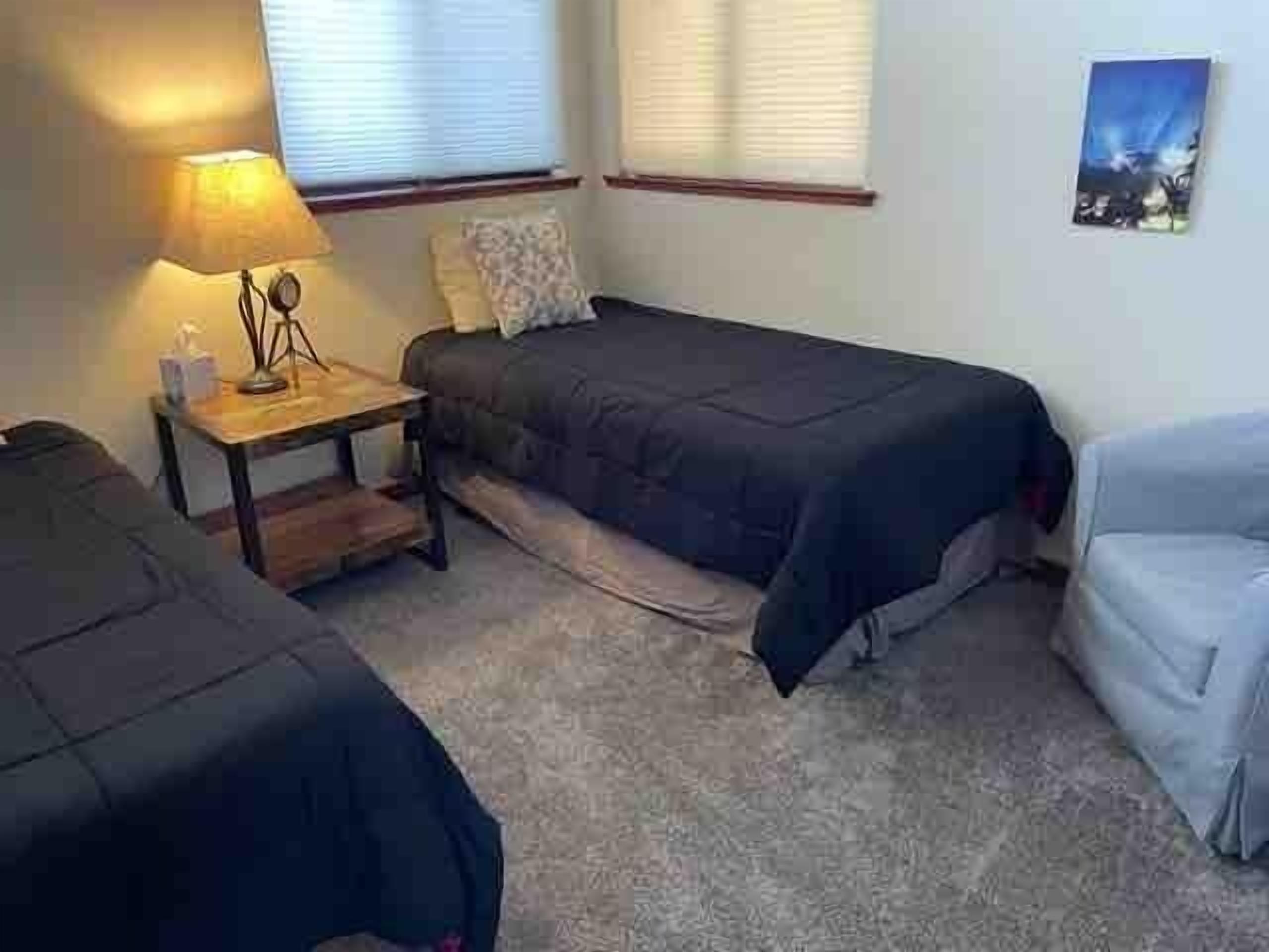 Une chambre avec deux lits simples, une table de chevet avec une lampe et une fenêtre avec des stores.