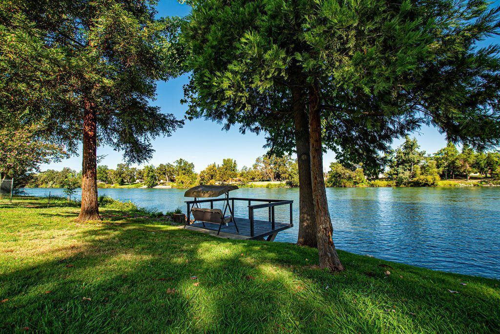 A lakeside deck with a swing chair, surrounded by trees and a clear view of the lake.