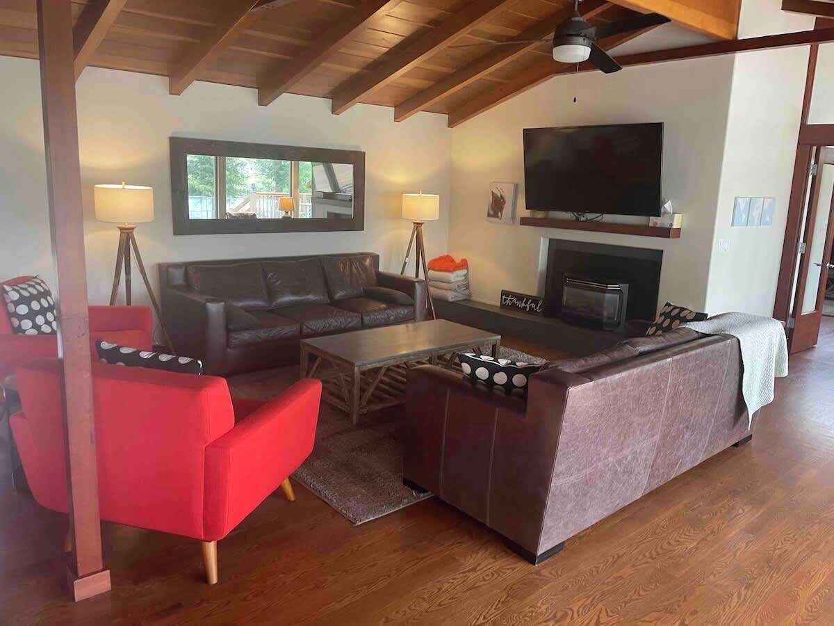 Ein Wohnzimmer mit einer Couch, roten Sesseln, einem Couchtisch, einem Kamin und einem an der Wand montierten Fernseher.
