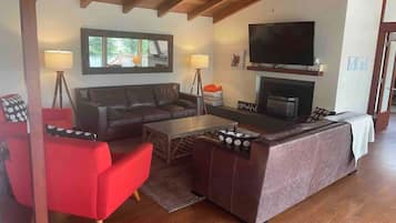 Ein Wohnzimmer mit einer Couch, roten Sesseln, einem Couchtisch, einem Kamin und einem an der Wand montierten Fernseher.