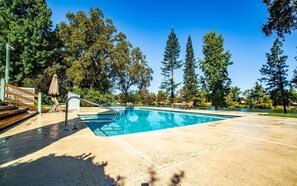 A swimming pool with a wooden deck, metal ladder, and lounge chairs.
