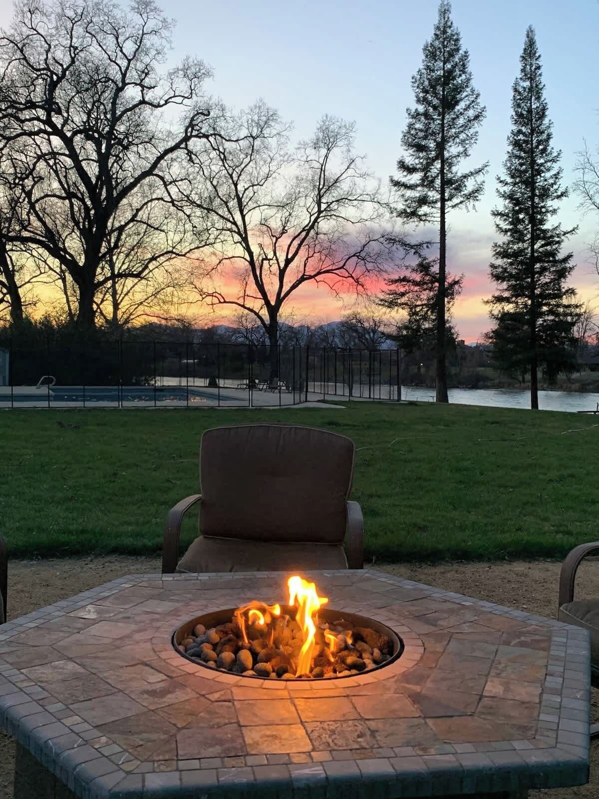 A fire pit with a chair in front, surrounded by a grassy area and trees.