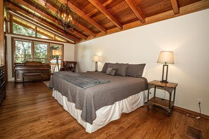 A bedroom with a large bed, wooden flooring, a bench, and a chandelier.
