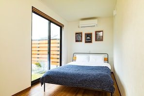 A bedroom with a bed, a large window, and a view of a building outside. - Cottage:Di Musica (Fujikawaguchiko)