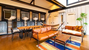 A modern living room with a wooden dining table, leather sofa, and a hammock. - Cottage:Di Musica (Fujikawaguchiko)