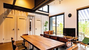 A dining area with a large wooden table, chairs, a television, and a view of the outdoors. - Cottage:Di Musica (Fujikawaguchiko)