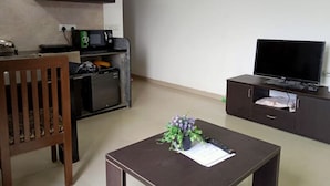 A compact living space with a kitchenette, a flat-screen TV, a small table with a plant, and a wooden chair. - Comfort of Home with Nature at its best (Khopoli)