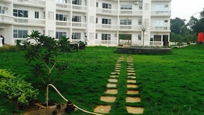 A multi-story white building with balconies and a paved pathway leading to the entrance. - Comfort of Home with Nature at its best (Khopoli)