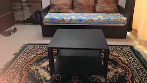 A room with a sofa against a wall, a small black table in the center, and a patterned rug on the floor. - Comfort of Home with Nature at its best (Khopoli)