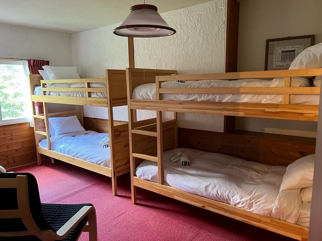 A room with bunk beds, a wooden desk, and a hanging lamp.