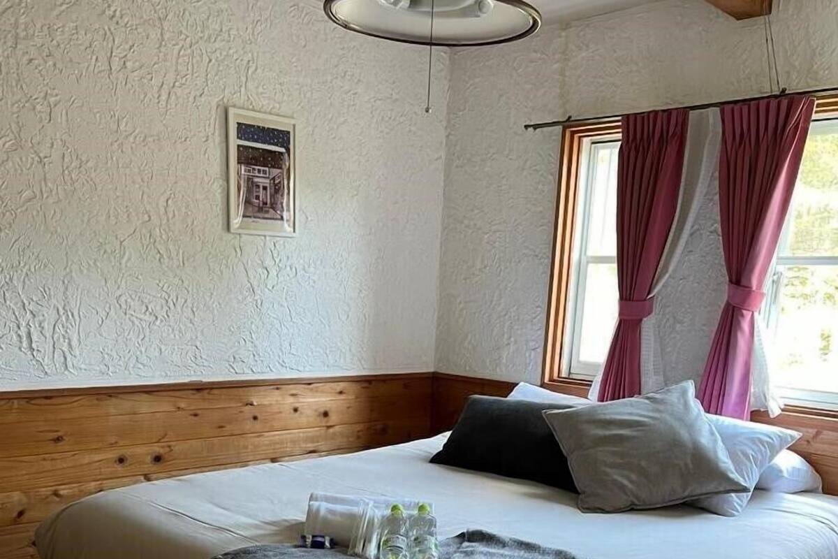 A bedroom with a wooden headboard, a bed with white bedding, a grey throw blanket, and a bedside table with water bottles.