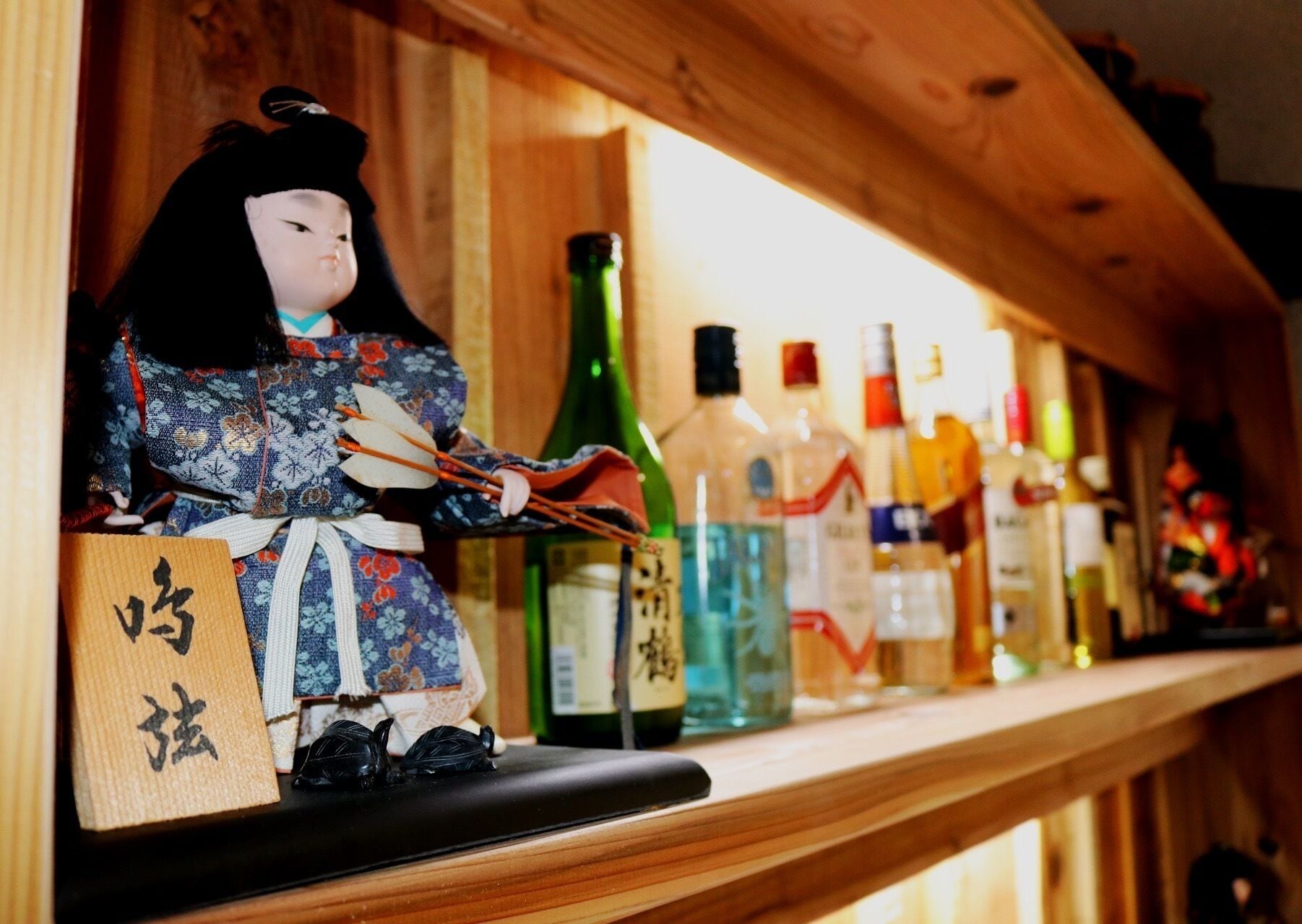 Una estantería con varias botellas y una muñeca tradicional japonesa.