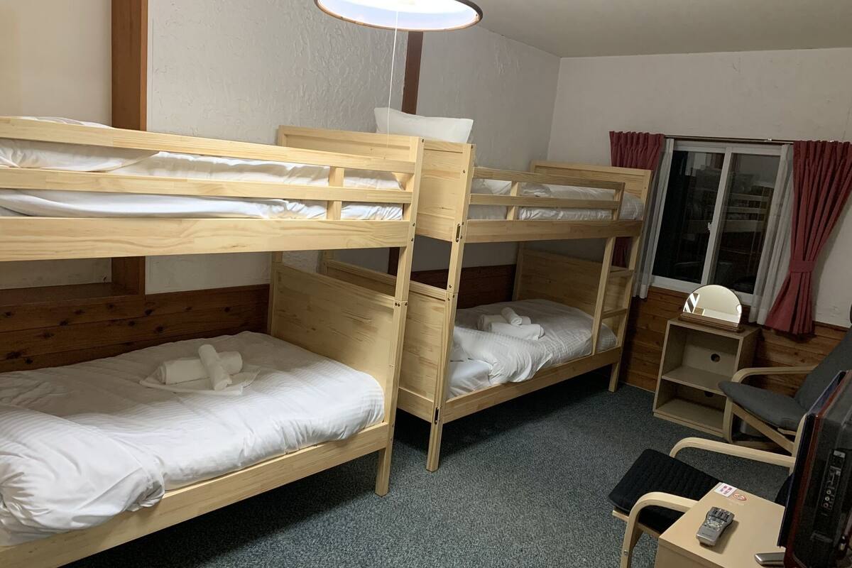 A room with two bunk beds, a desk with a chair, a TV, and a window with curtains.