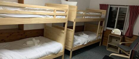 A room with two bunk beds, a desk with a chair, a TV, and a window with curtains.