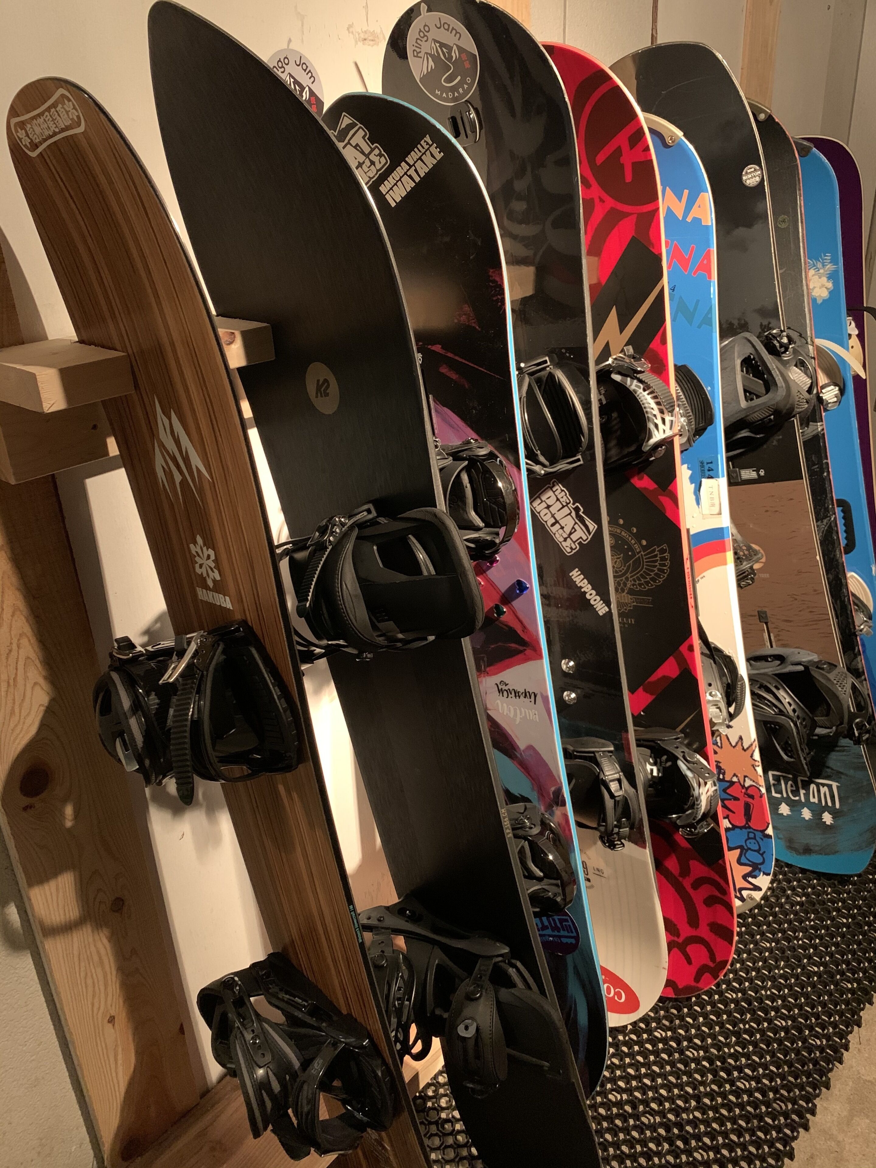 Várias pranchas de snowboard penduradas na parede, cada uma com designs e logotipos distintos.