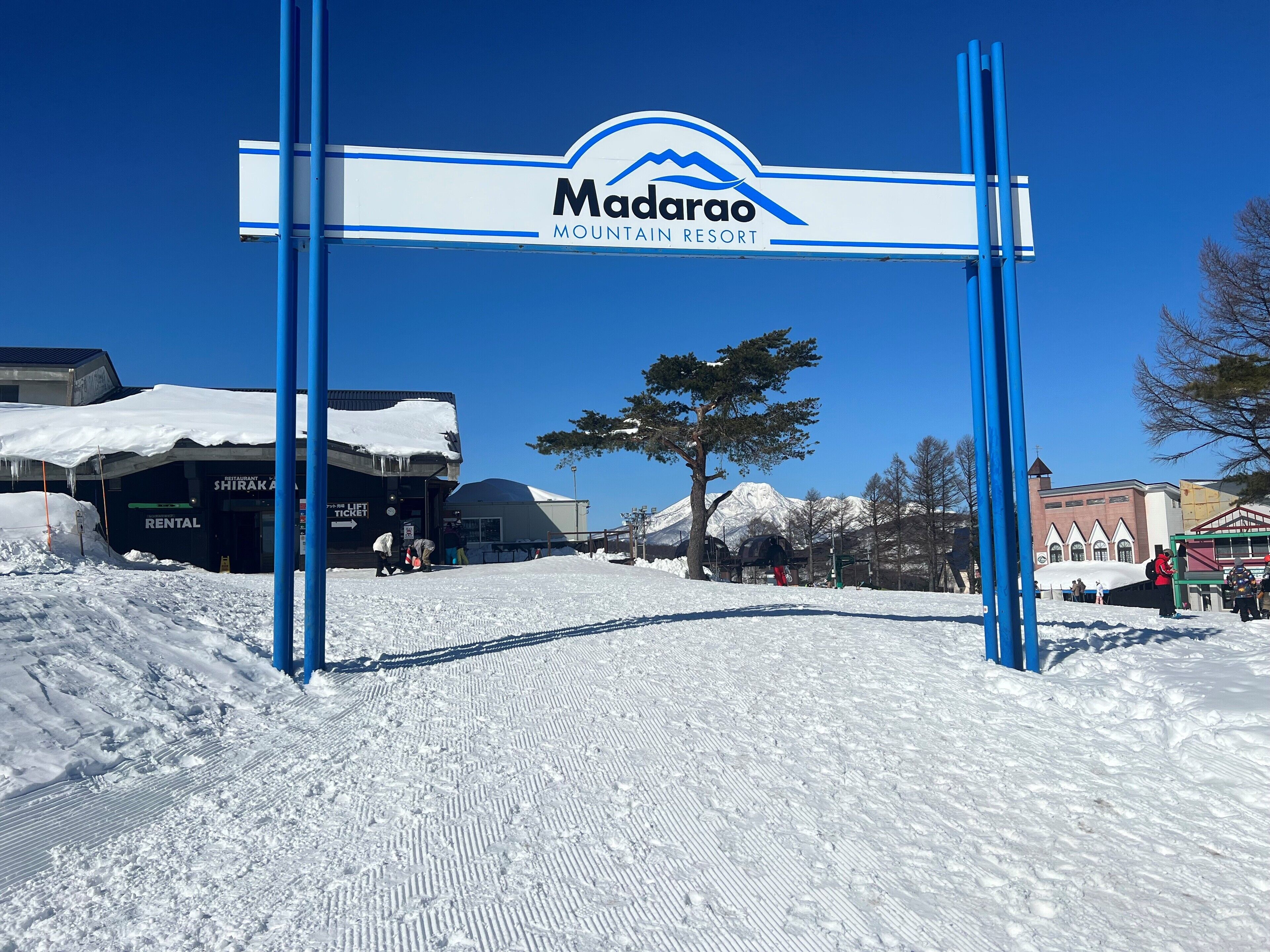 A snow-covered entrance to Madarao Mountain Resort with a signboard, a rental building, and a mountain in the background.