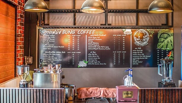 A coffee shop interior with a menu board, espresso machines, and a counter. - Sleep Box Hostel Suratthani (Surat Thani)