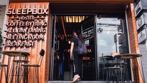 A storefront with a sign listing services such as a sleepbox, hostel, coffee by bung, all-day dining, meeting room, and breakfast. - Sleep Box Hostel Suratthani (Surat Thani)