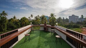 A rooftop terrace with artificial grass, seating, and a view of palm trees and buildings. - Sleep Box Hostel Suratthani (Surat Thani)