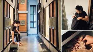 A hallway with a wooden floor, air conditioning units, and a person sitting at a desk with a laptop. - Sleep Box Hostel Suratthani (Surat Thani)