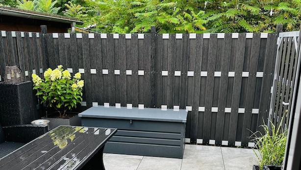 Un espace patio aménagé avec une table en métal noir, un banc et des meubles en osier.