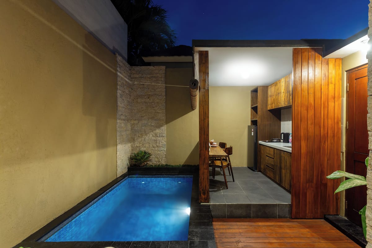A modern outdoor pool area with a stone wall, wooden deck, and a small dining table.