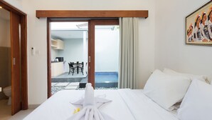 A hotel room with a bed, a bathroom, and a view of a pool and outdoor seating area. - Radea Villa (Kerobokan)