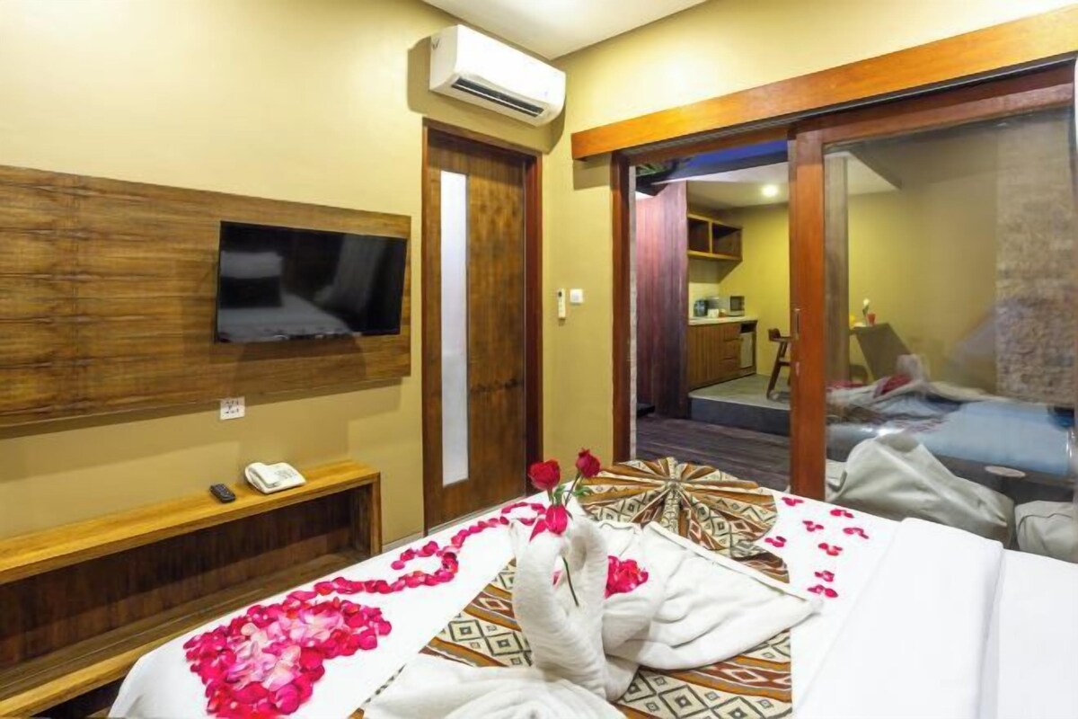 A hotel room with a bed, a TV mounted on the wall, a bedside table with a phone, and a mirror.