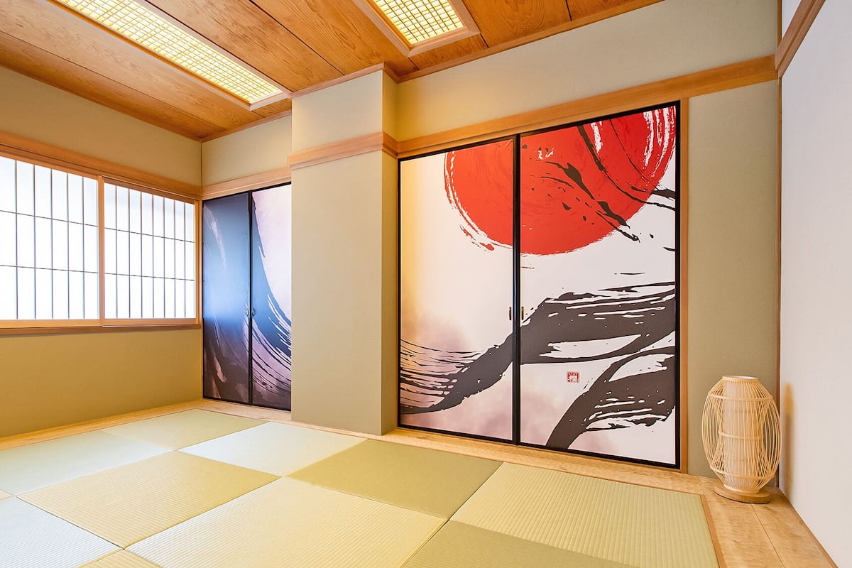 A traditional Japanese room with tatami flooring, sliding doors, and artwork on the walls.