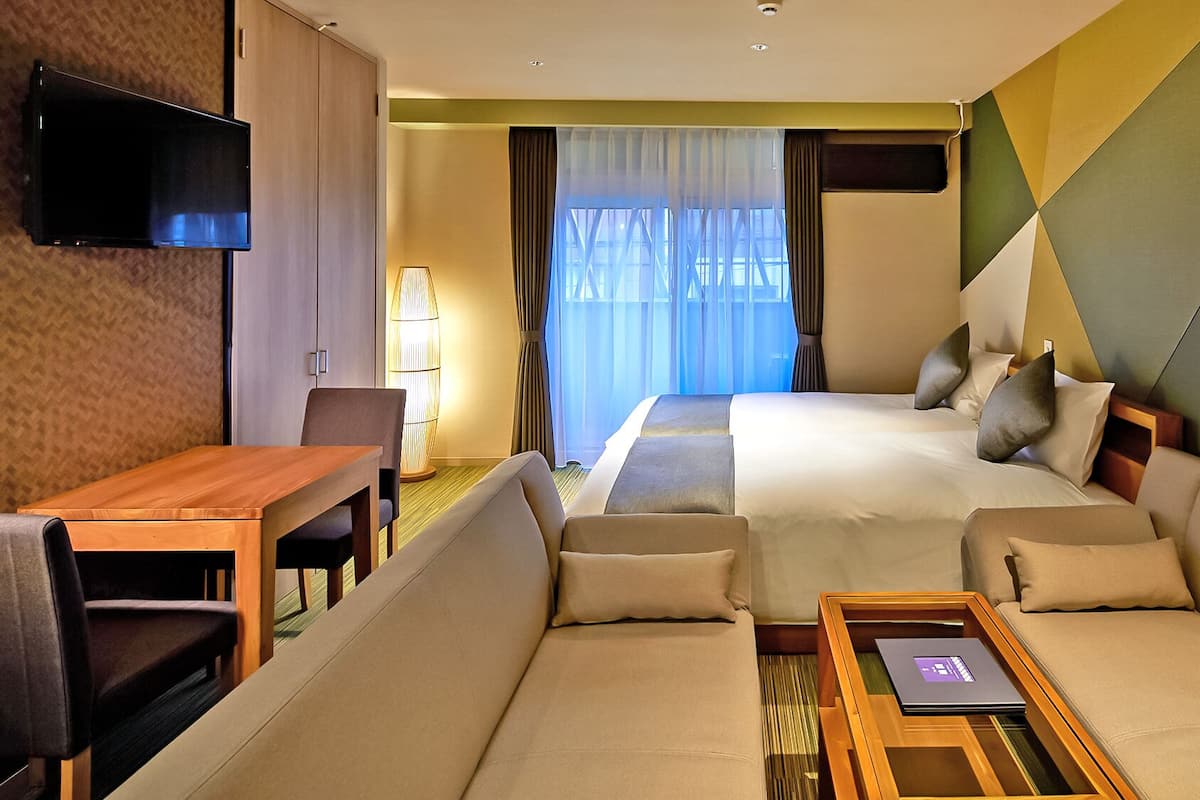 A hotel room with a bed, sofa, TV, and a table with a laptop.