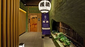 Un pasillo de hotel con estética japonesa tradicional, que presenta una puerta de madera con un mural, un letrero del Asakusa Hotel y un farol.