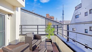 Un balcón con mobiliario de mimbre, una planta en maceta y una torre al fondo.