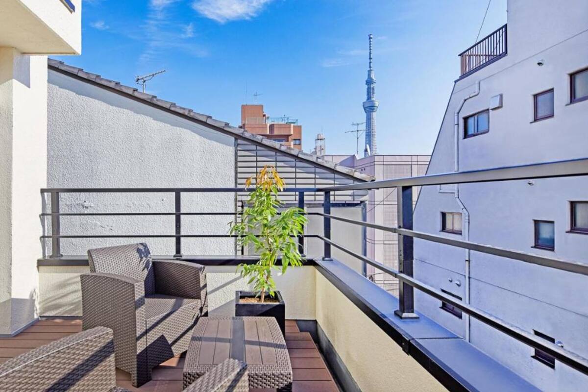 A balcony with wicker furniture, a potted plant, and a view of a tower in the background.