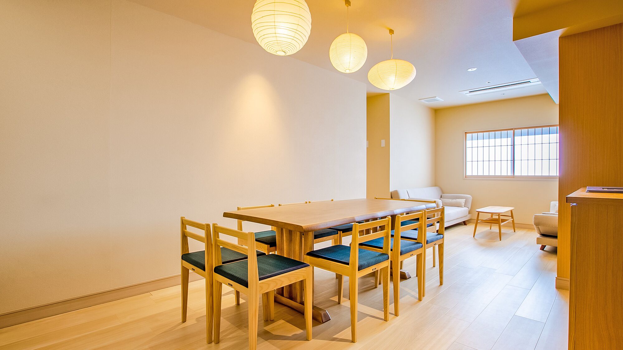 A dining area with a wooden table and chairs, a sofa, and a window with blinds.