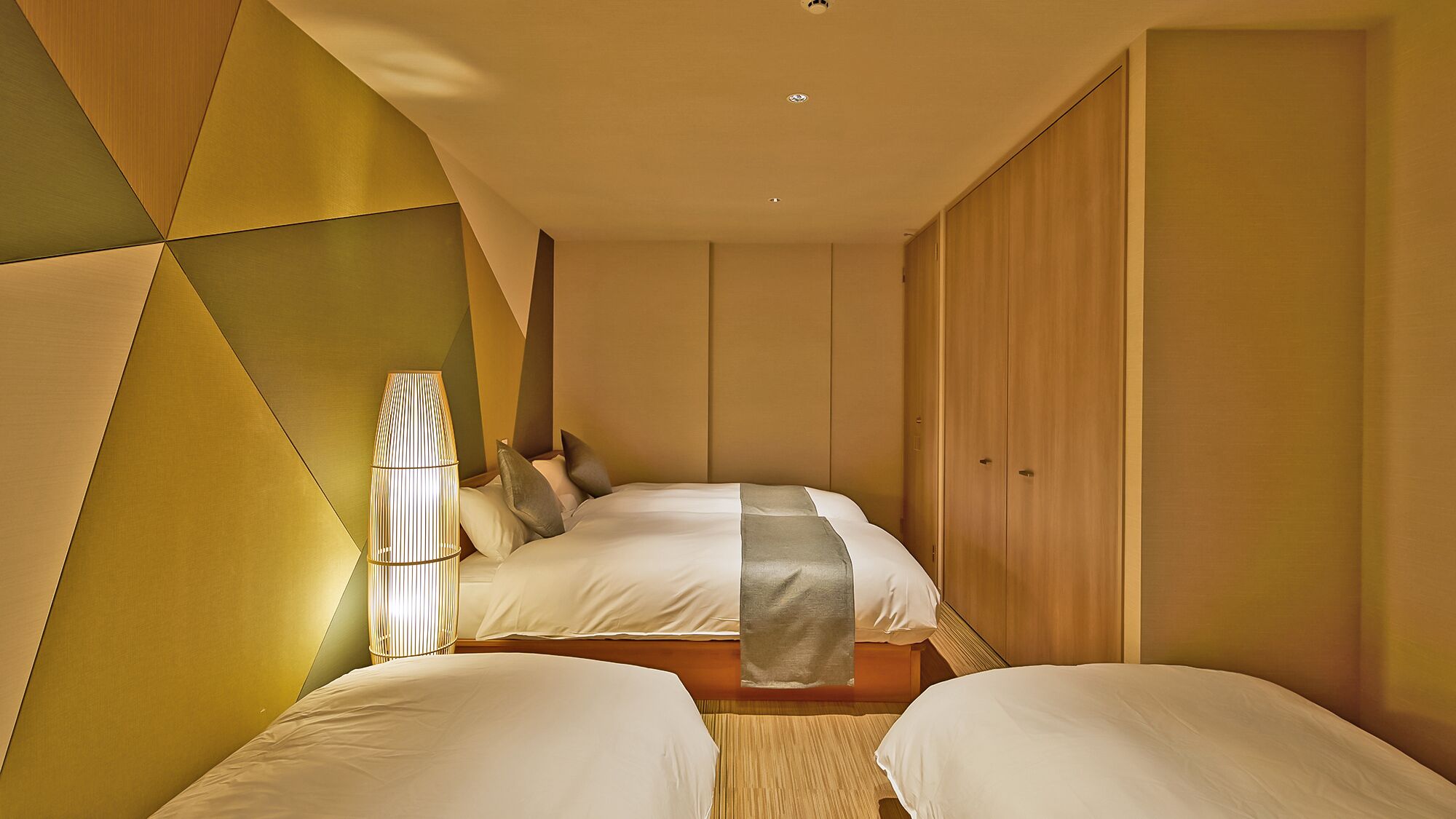 A modern bedroom with a geometric wall design, a bed with white bedding, and a bedside lamp.