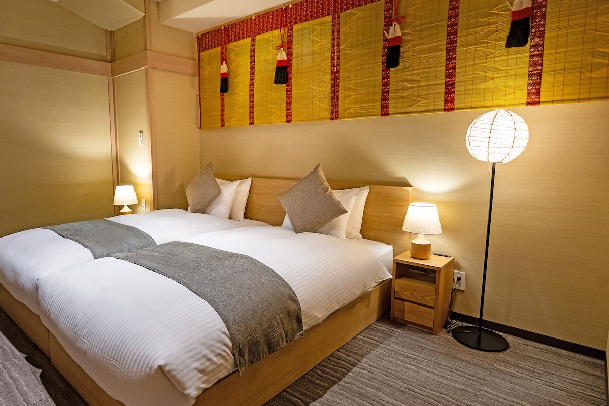 A hotel room with a large bed, two bedside tables, a floor lamp, and a decorative wall panel.