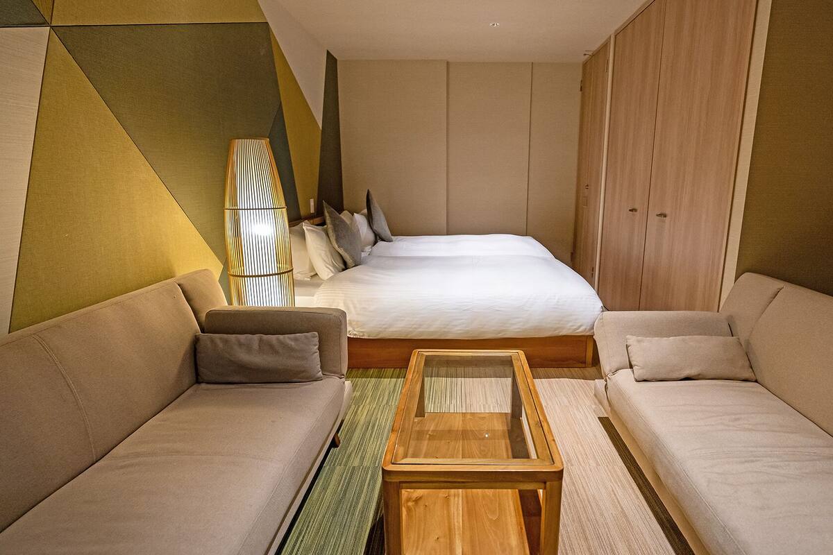 A modern hotel room with a large bed, two sofas, a wooden coffee table, and a geometric-patterned wall.