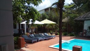 A pool area with lounge chairs and umbrellas, surrounded by greenery and a building in the background. - Suoi Tien Mui Ne Resort (Mui Ne)